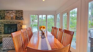 A dining area with a stone fireplace, large windows, and a table set for six.