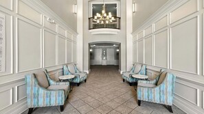 A hotel lobby with a high ceiling, a chandelier, and a central door leading to another room. There are two seating areas with patterned chairs and small tables. - Huge Vista Cay Ground Floor (Orlando)