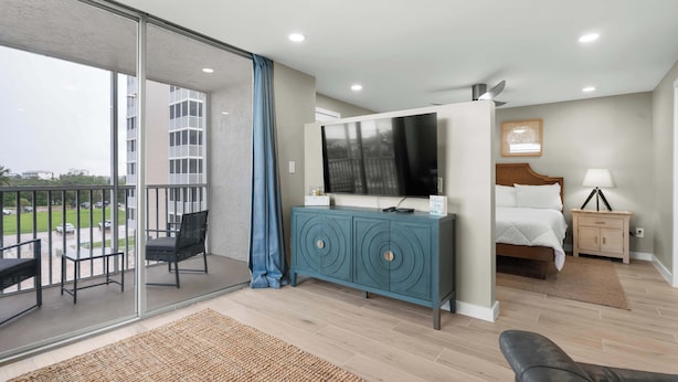 A hotel room with a balcony, a TV, a bed, a nightstand, and a sofa. - Newly Renovated Beach & Tennis Unit 3402 (Bonita Springs)