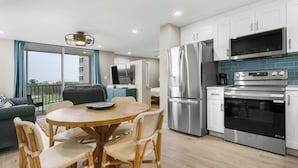 A modern kitchen with stainless steel appliances, a dining area with wicker chairs, and a balcony with a view. - Newly Renovated Beach & Tennis Unit 3402 (Bonita Springs)