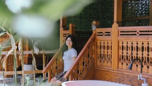 Una mujer sentada en una escalera de madera en una habitación con una bañera grande llena de agua y pétalos de flores.