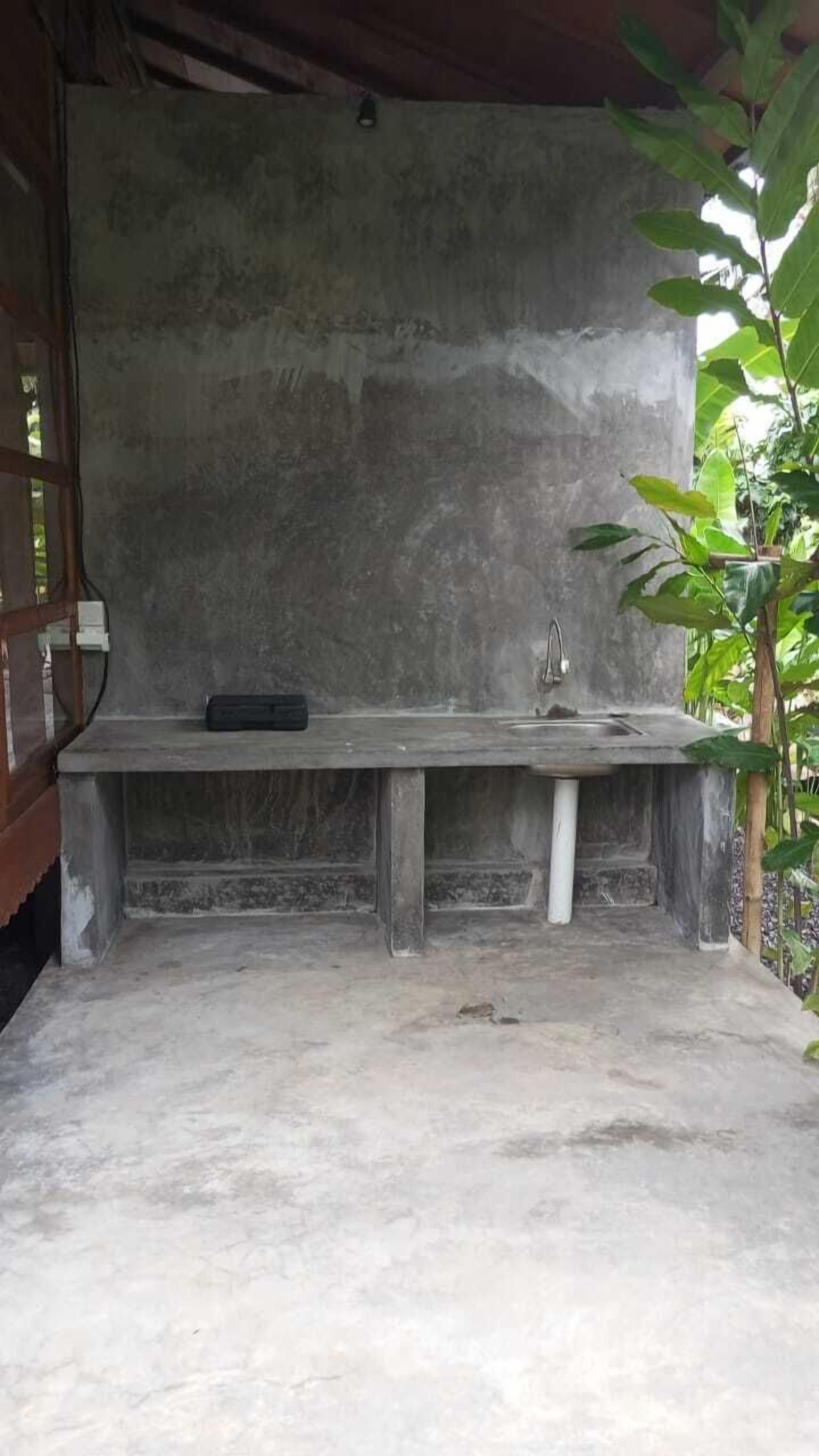 Een betonnen bank met een wasbak en kraan, omringd door groen.
