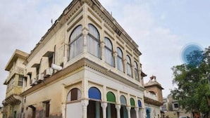 Un edificio histórico con entrada en esquina, amplias ventanas arqueadas y un balcón con barandilla.