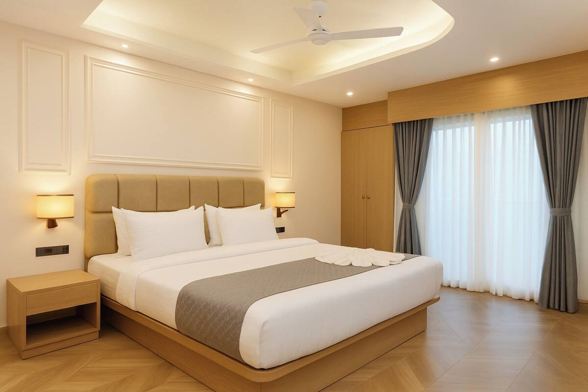 Une chambre d’hôtel moderne dotée d’un grand lit, de lampes de chevet, d’un ventilateur de plafond et offrant une vue sur l’extérieur grâce à de grandes fenêtres.