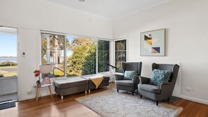 Una sala de estar moderna con un sillón gris, un sofá y un ventanal con vistas a árboles y un edificio.
