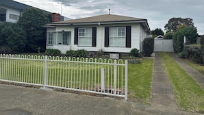 Une maison de plain-pied à l’extérieur blanc, avec des volets sombres, un jardin devant la maison délimité par une clôture blanche et une allée menant au garage.