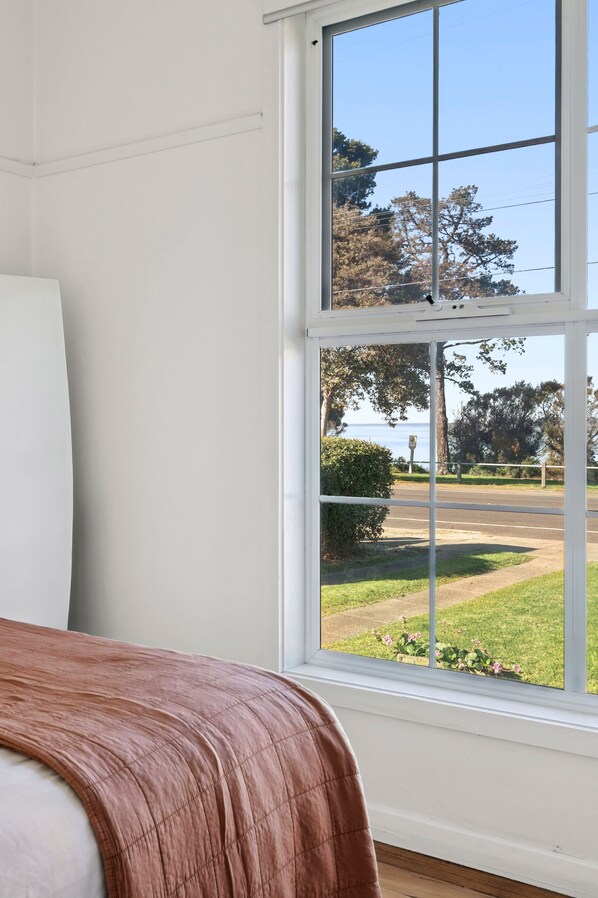 A room with a large window offering a view of a street and greenery.