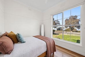 A bedroom with a large window, a bed with multiple pillows, and a white wall.