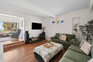 Una sala de estar moderna con un sofá verde, un televisor de pantalla plana y un gran ventanal con vistas a un balcón.