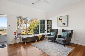 A modern living room with a grey armchair, a sofa, and a large window offering a view of trees and a building.