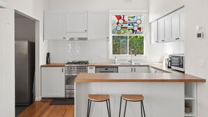 Una cocina moderna con armarios blancos, encimera de madera, horno integrado y ventana con un diseño de vidrio emplumado de colores.