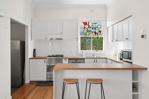 A modern kitchen with white cabinets, a wooden countertop, a built-in oven, and a window with a colorful stained glass design.