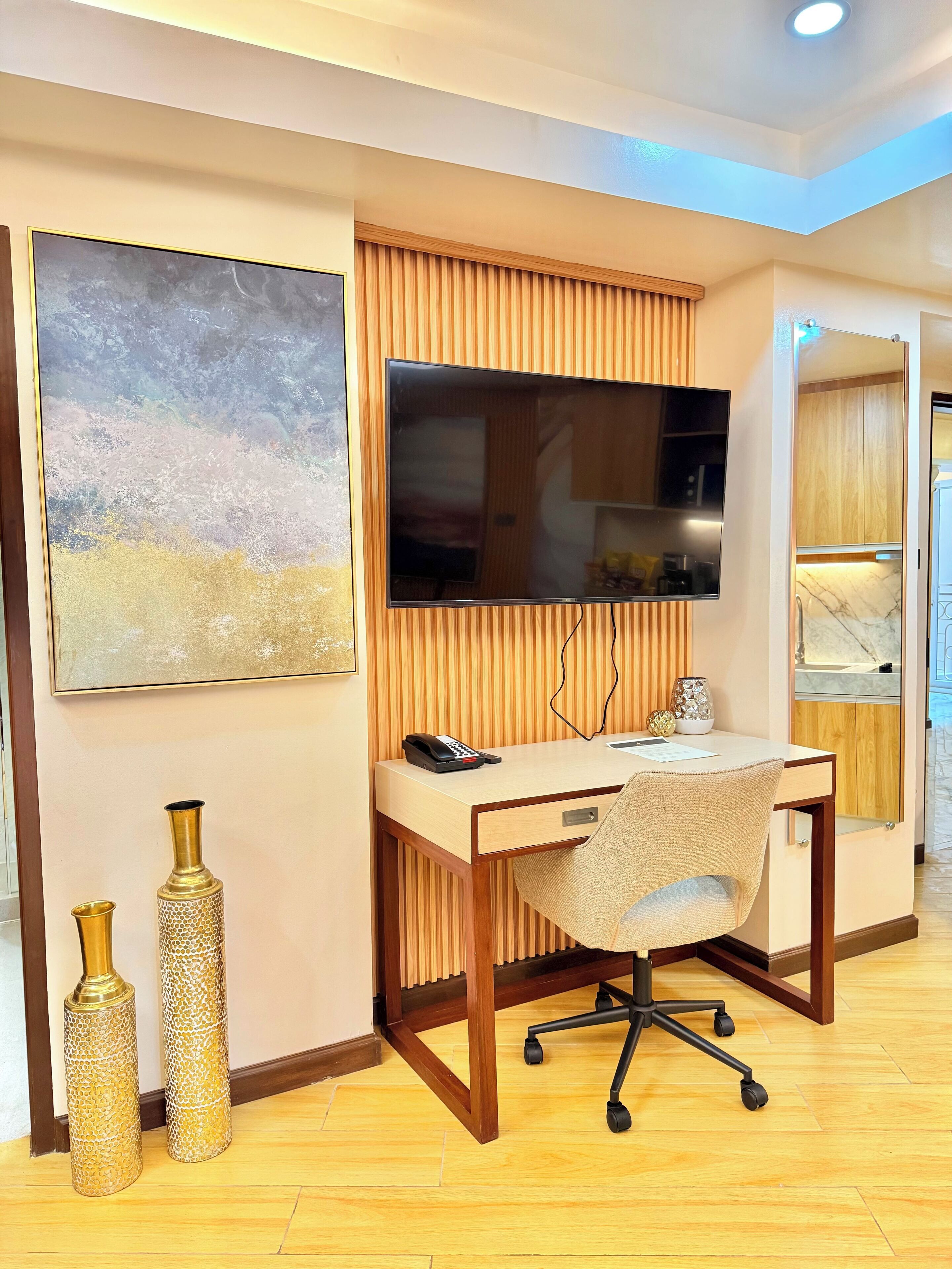 A modern office space with a desk, chair, mounted TV, and decorative vases.