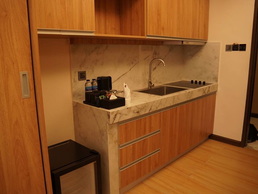 Une cuisine compacte dotée d’un plan de travail en marbre, de meubles en bois, d’un évier encastré et d’un petit réfrigérateur.