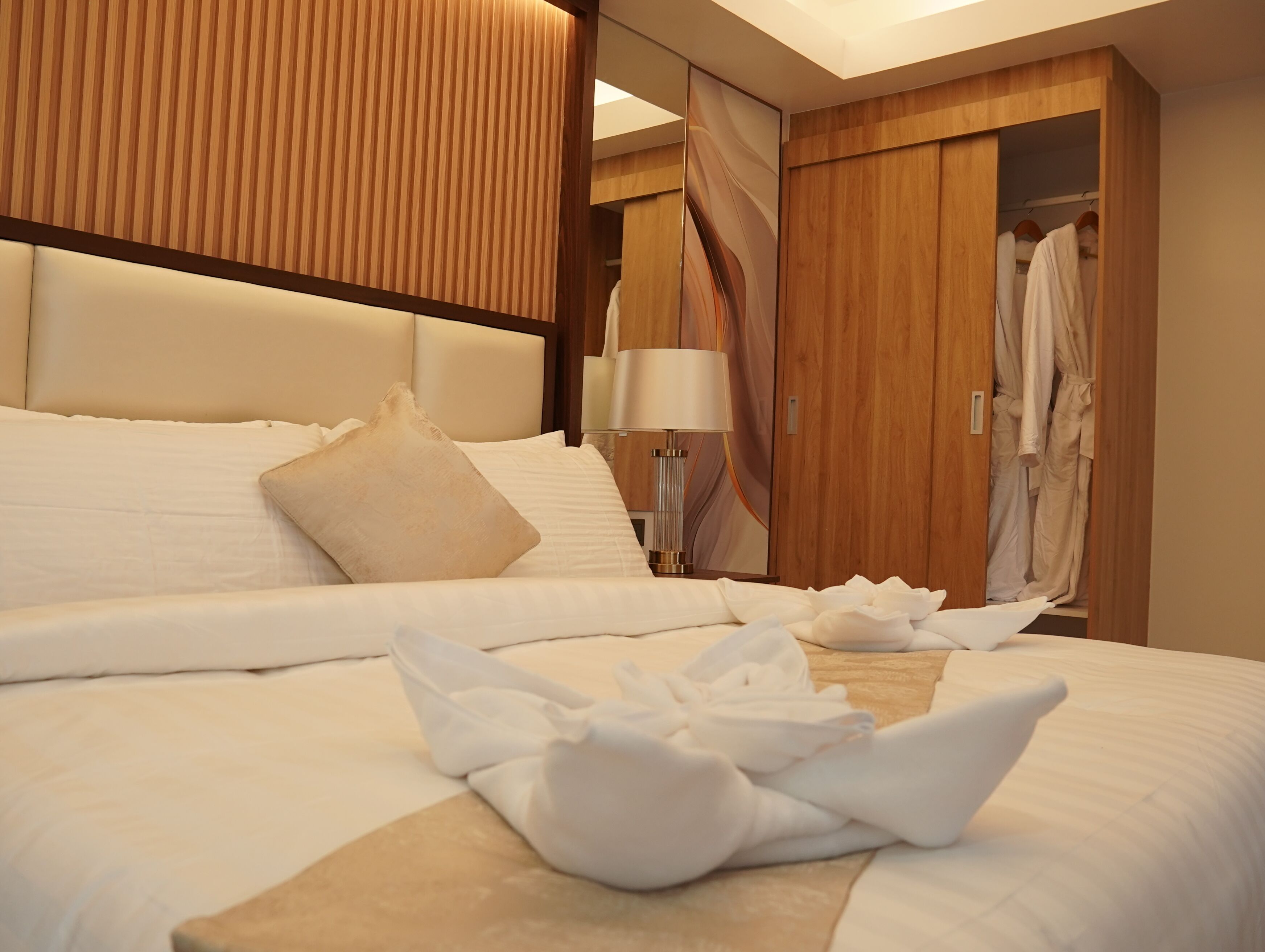 Une chambre d’hôtel avec un grand lit, une tête de lit en bois, une table de chevet avec une lampe et une armoire avec des peignoirs.