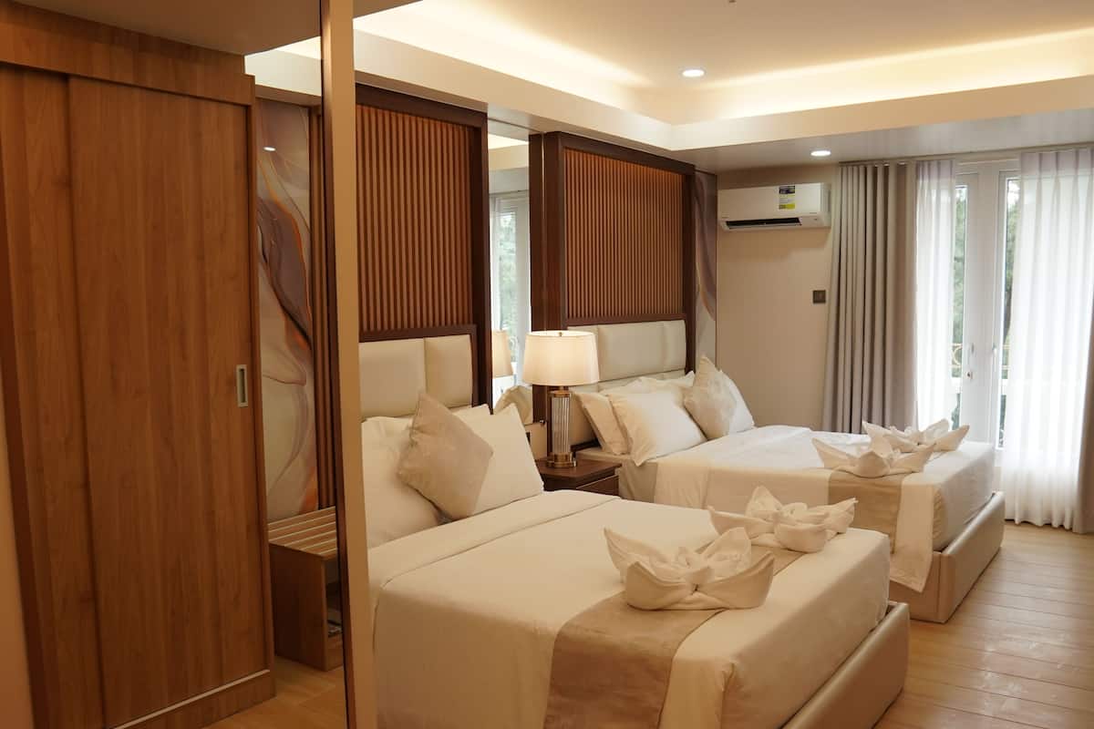 Une chambre d’hôtel avec deux lits, un plancher en bois, une armoire et un appareil de climatisation.