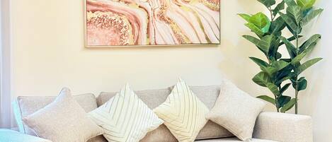 A living room with a beige sofa, a marble artwork, a green plant, and a small round table with gold legs.