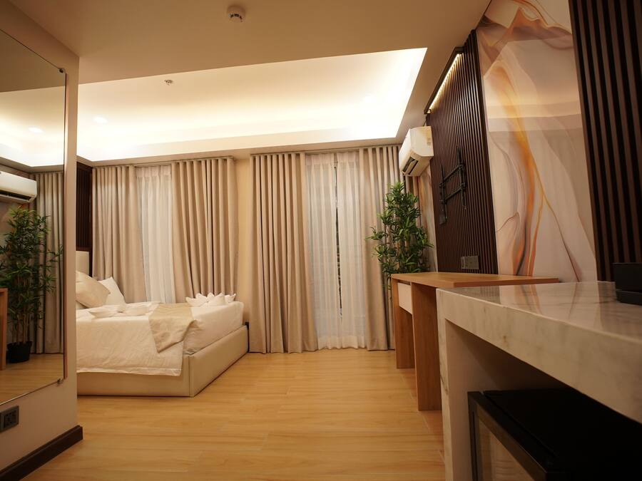 Una habitación de hotel moderna con una cama grande, un escritorio y un amplio ventanal con cortinas.