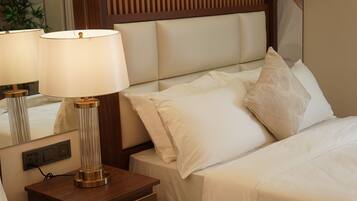 A neatly made bed with white linens and a headboard with vertical slats. There is a bedside table with a lamp and a mirror.