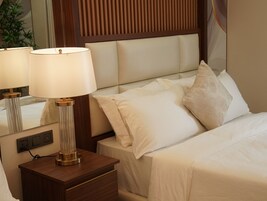 A neatly made bed with white linens and a headboard with vertical slats. There is a bedside table with a lamp and a mirror.