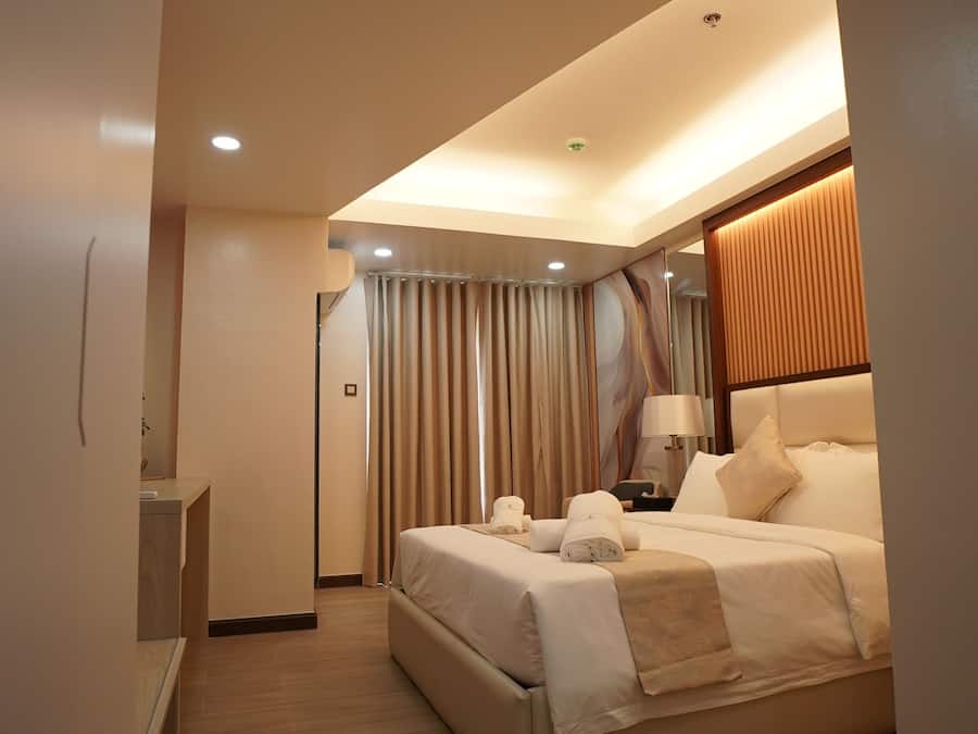 Habitación de hotel moderna con una cama grande, una mesita de noche, una lámpara y vistas al exterior a través de las cortinas.