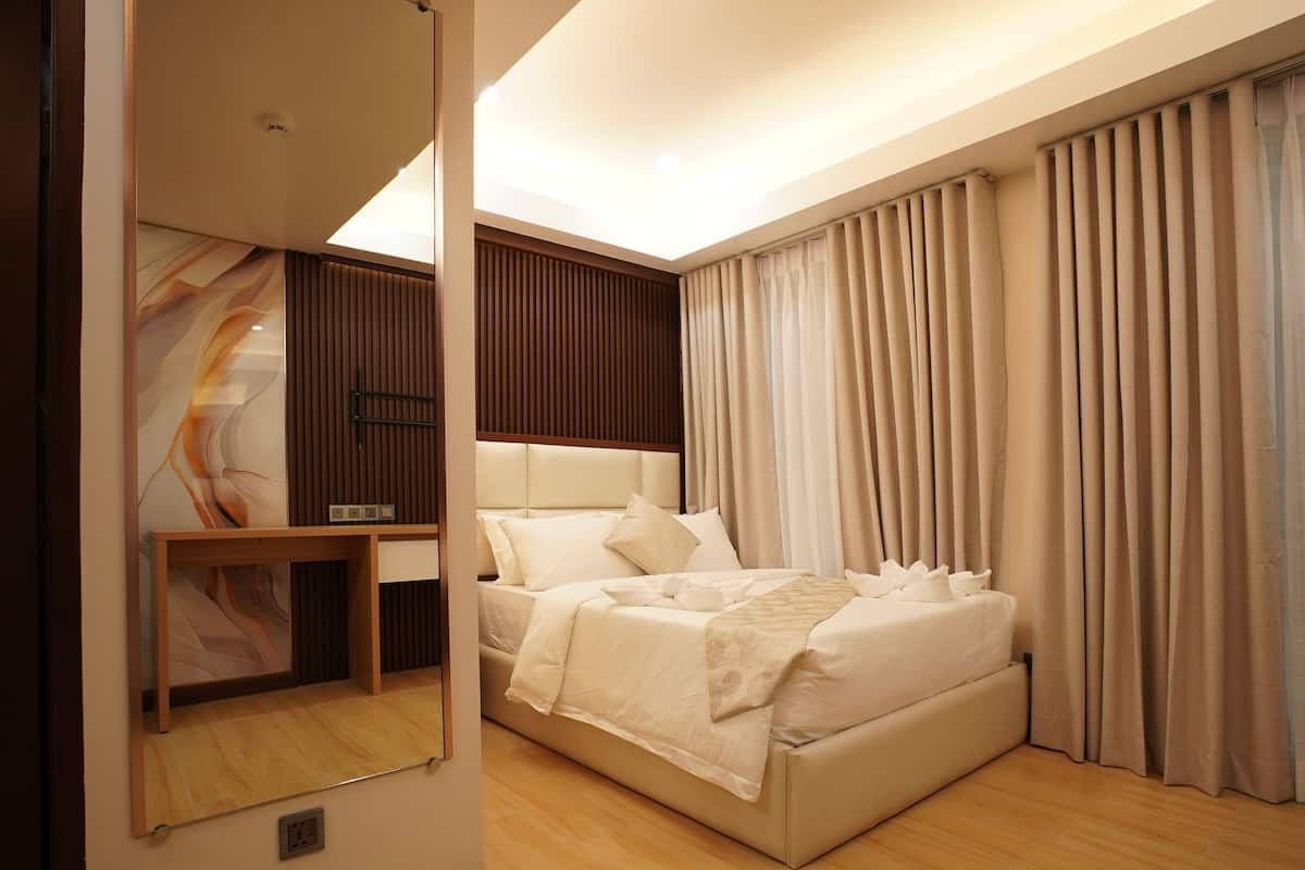 Une chambre moderne avec un grand lit, une table de chevet, un miroir et une vue sur l’extérieur à travers des rideaux.