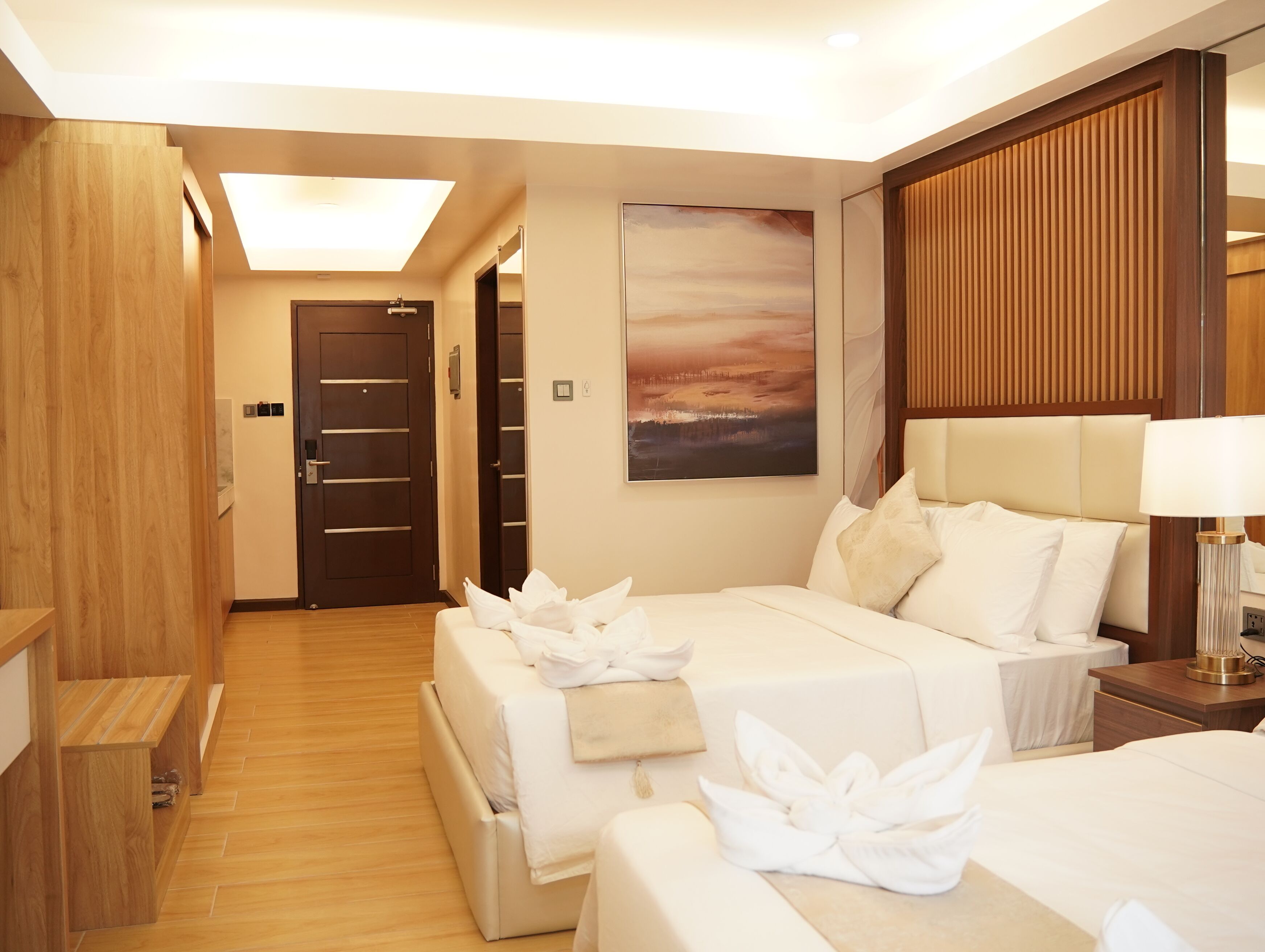 Habitación de hotel con dos camas, suelo de madera, un cuadro grande y un panel de pared de madera.