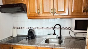 A kitchen with wooden cabinets, a stainless steel sink, a coffee maker, a microwave, and a toaster. - Fuente del Tesoro Apartment (AN)