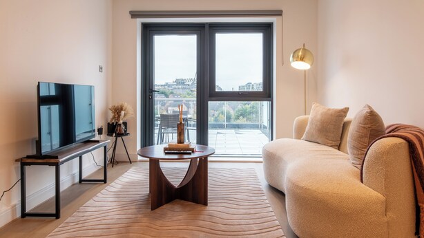 Una sala de estar moderna con un televisor de pantalla plana, una mesa de centro redonda, un sofá y un ventanal con vistas a la ciudad.