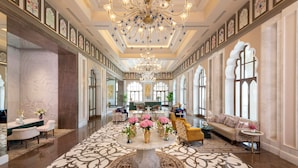 A spacious lobby with a central round table surrounded by sofas and chairs, large windows, and a chandelier. - Taj Lalit Bagh, Udaipur (Māvli)