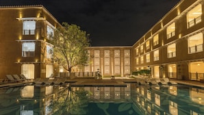 A pool area with lounge chairs and a reflection pool, surrounded by multi-story buildings with balconies and windows. - Taj Lalit Bagh, Udaipur (Māvli)