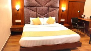 A hotel room with a large bed, two bedside lamps, a desk with a chair, and a wooden headboard. - ECKO Vasudeva (Joshimath)