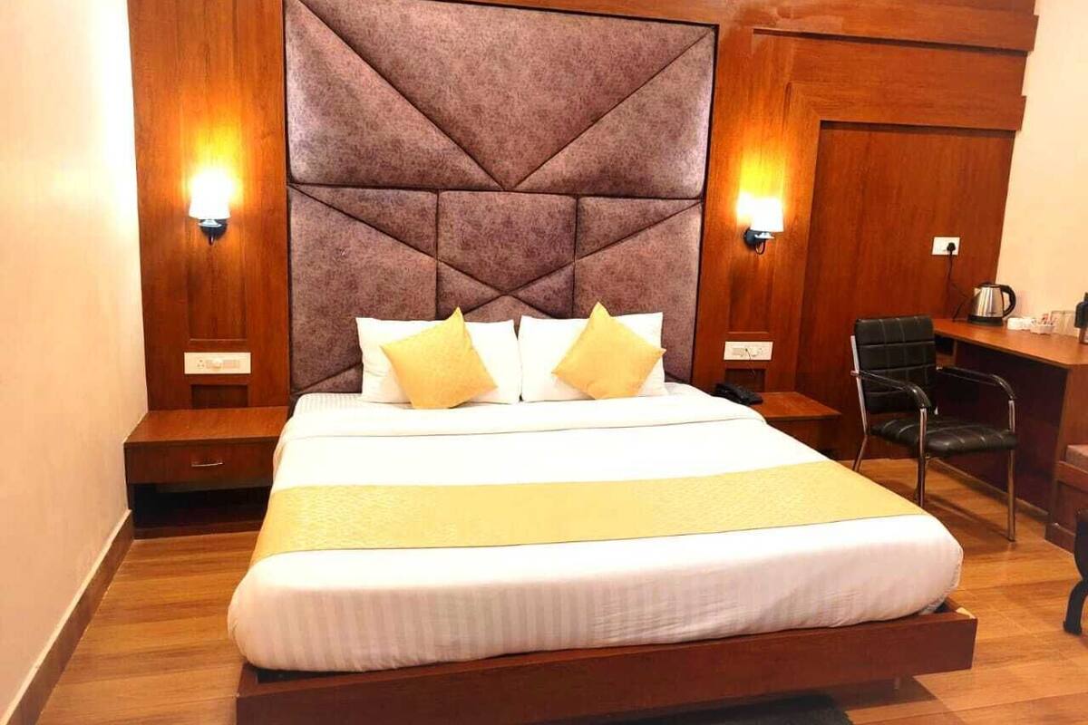 A hotel room with a large bed, two bedside lamps, a desk with a chair, and a wooden headboard.