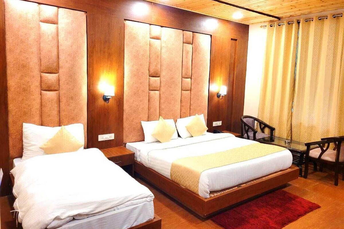 A hotel room with two beds, wooden headboards, wall-mounted lights, a small table, and a chair.