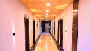 A long, well-lit hallway with a shiny floor, doors on both sides, and a central elevator. - ECKO Vasudeva (Joshimath)