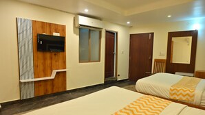 A hotel room with two beds, a mounted TV, a wooden panel wall, and a mirror. - Mysore Heritage Inn (Mysore)