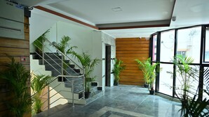 A modern lobby with a staircase, potted plants, and a large window offering a view of the outside. - Mysore Heritage Inn (Mysore)