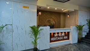 A reception desk with a sign reading "MYSORE HERITAGE INN" and a check-in/out time sign. - Mysore Heritage Inn (Mysore)