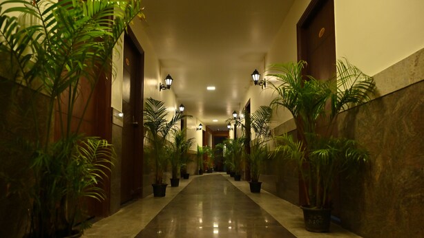 A hallway with potted plants, wooden doors, and wall-mounted lights. - Mysore Heritage Inn (Mysore)