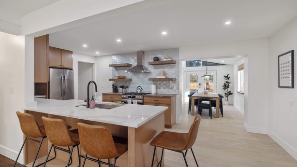 A modern kitchen with a central island, wooden cabinets, and a stainless steel refrigerator. - Renovated 7BR - Gym, Hot Tub, Sauna & Cold Plunge! (Southfield)