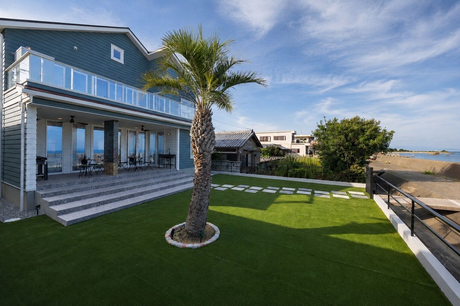 A modern house with a covered patio, a palm tree, and a view of the beach.
