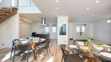 A modern kitchen with a dining area, featuring a glass table, wicker chairs, and a staircase.