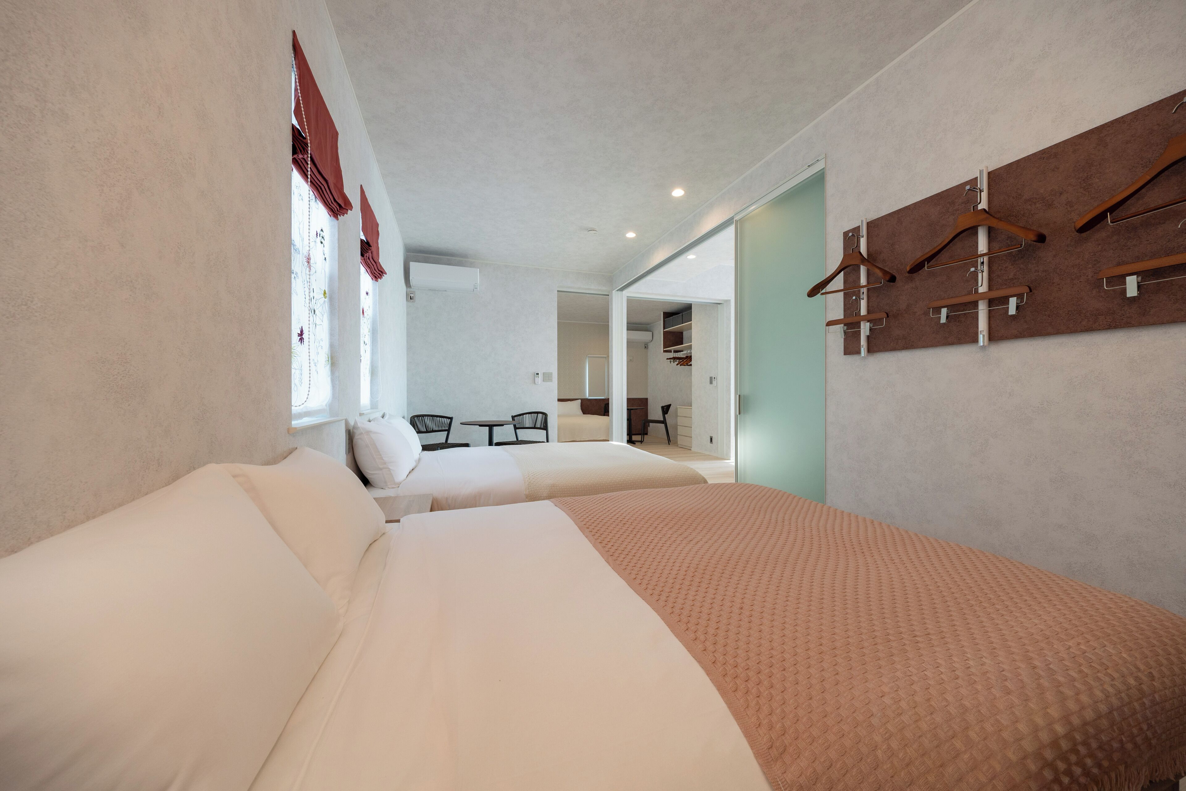 A hotel room with two beds, a wardrobe, and a seating area with chairs and a table.