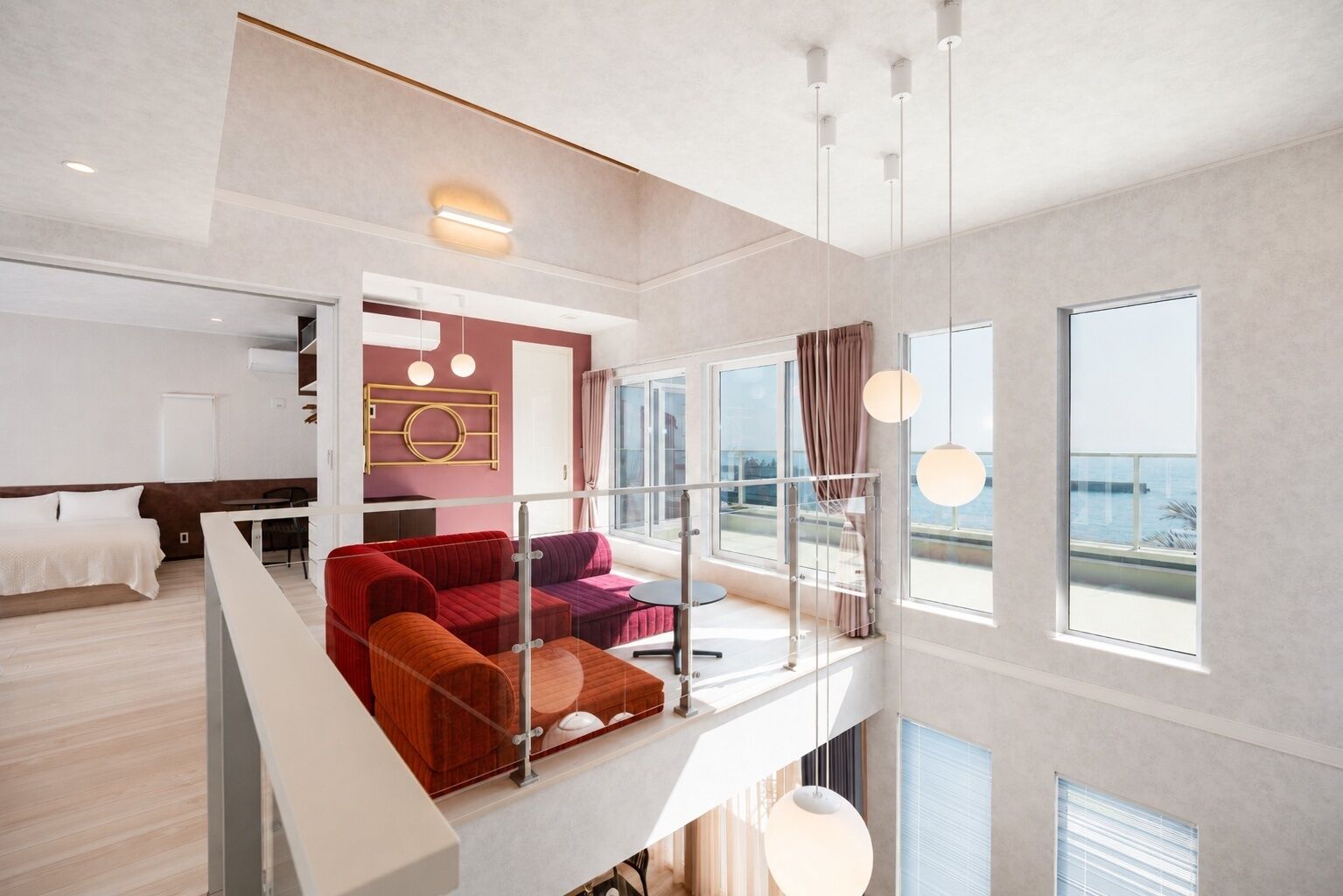 Ett modernt hotellrum med en balkong, en säng, en sittgrupp med en röd soffa och stora fönster med utsikt.