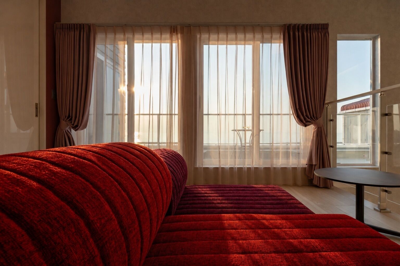 Une pièce avec un canapé rouge, une petite table et un balcon doté d’une balustrade.