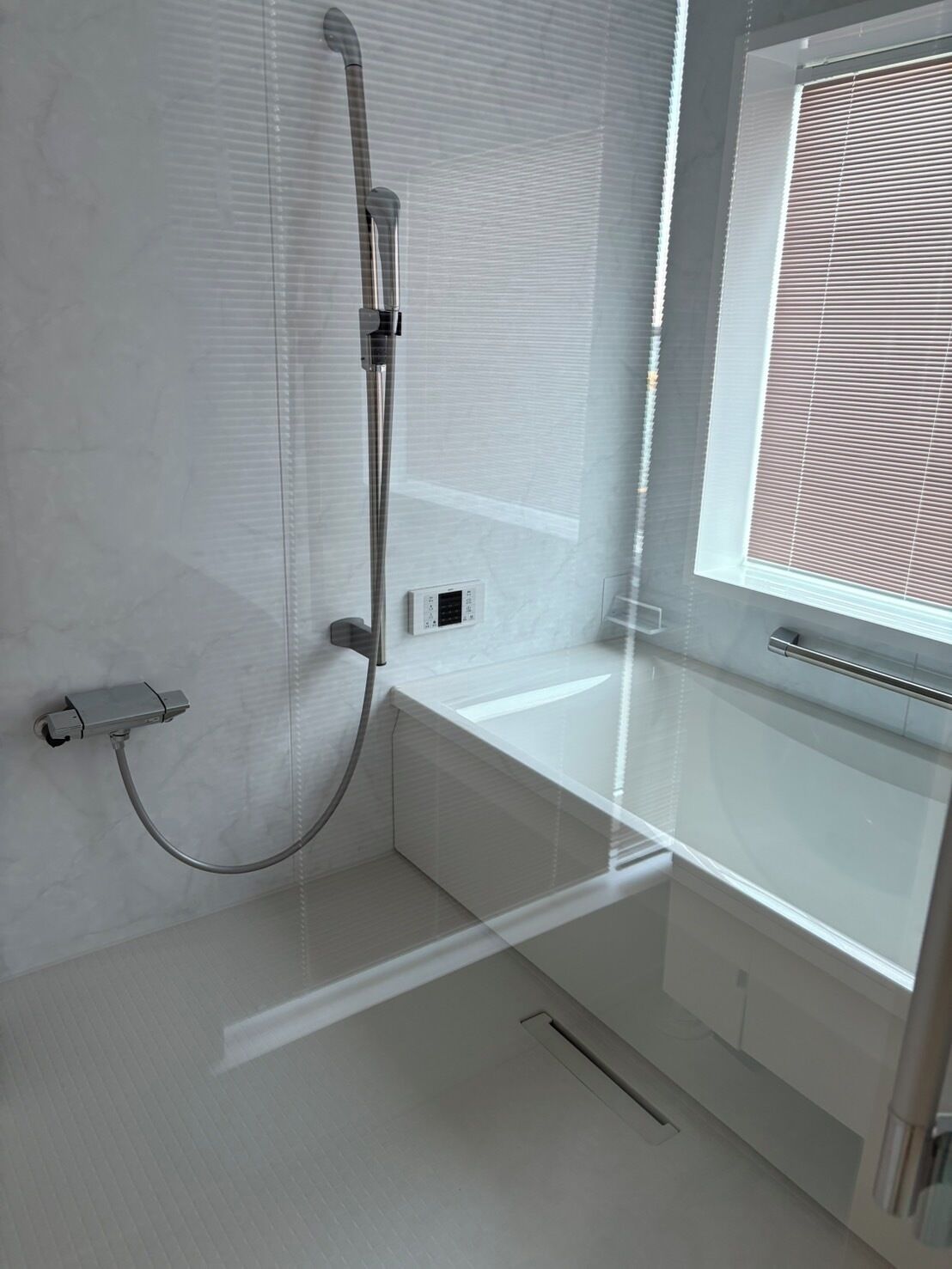A modern bathroom with a glass shower enclosure, a built-in sink, and a window with blinds.