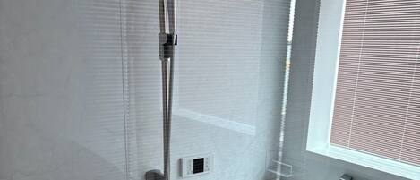 A modern bathroom with a glass shower enclosure, a built-in sink, and a window with blinds.