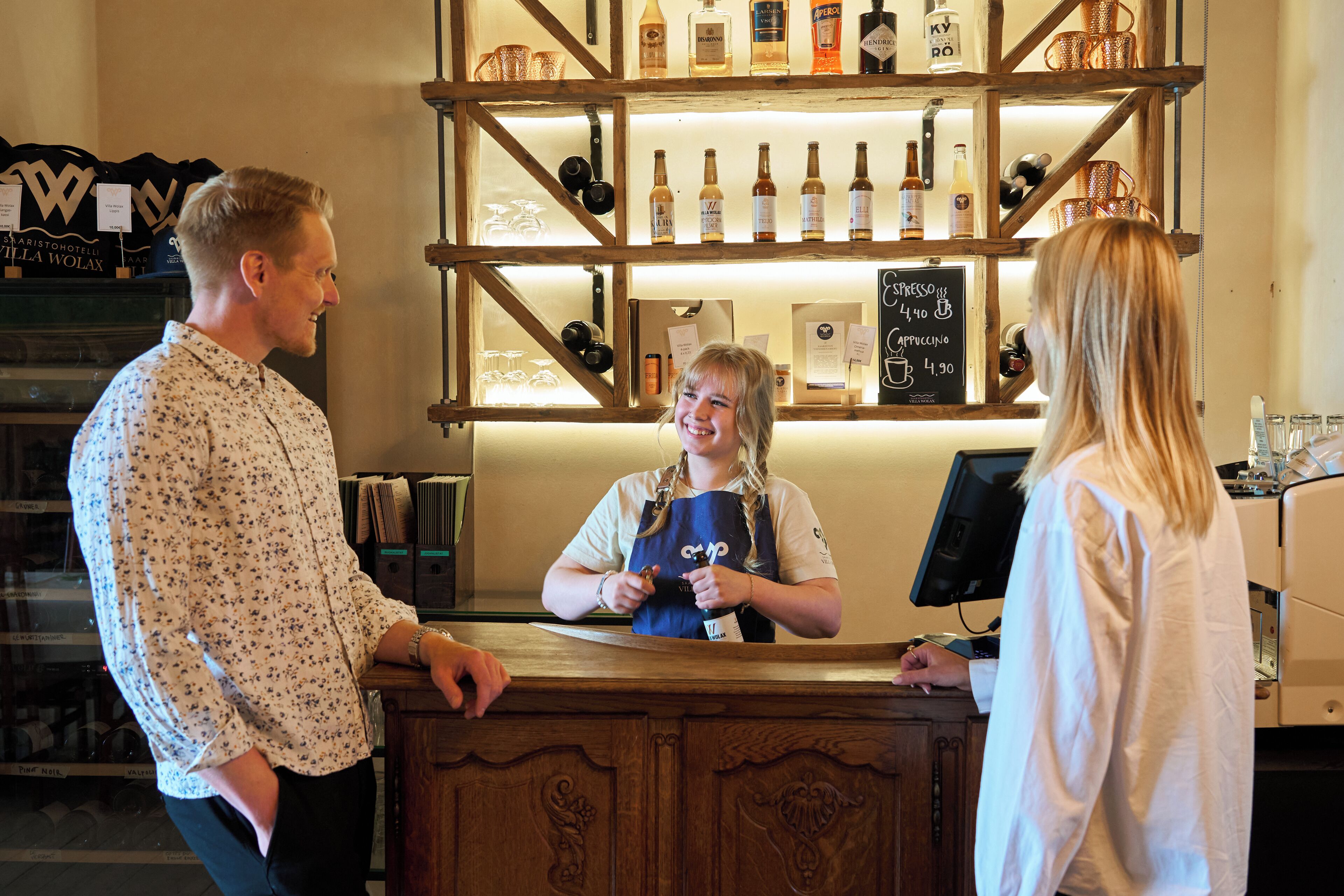 A bar area with a wooden counter, shelves with bottles, and a chalkboard menu.