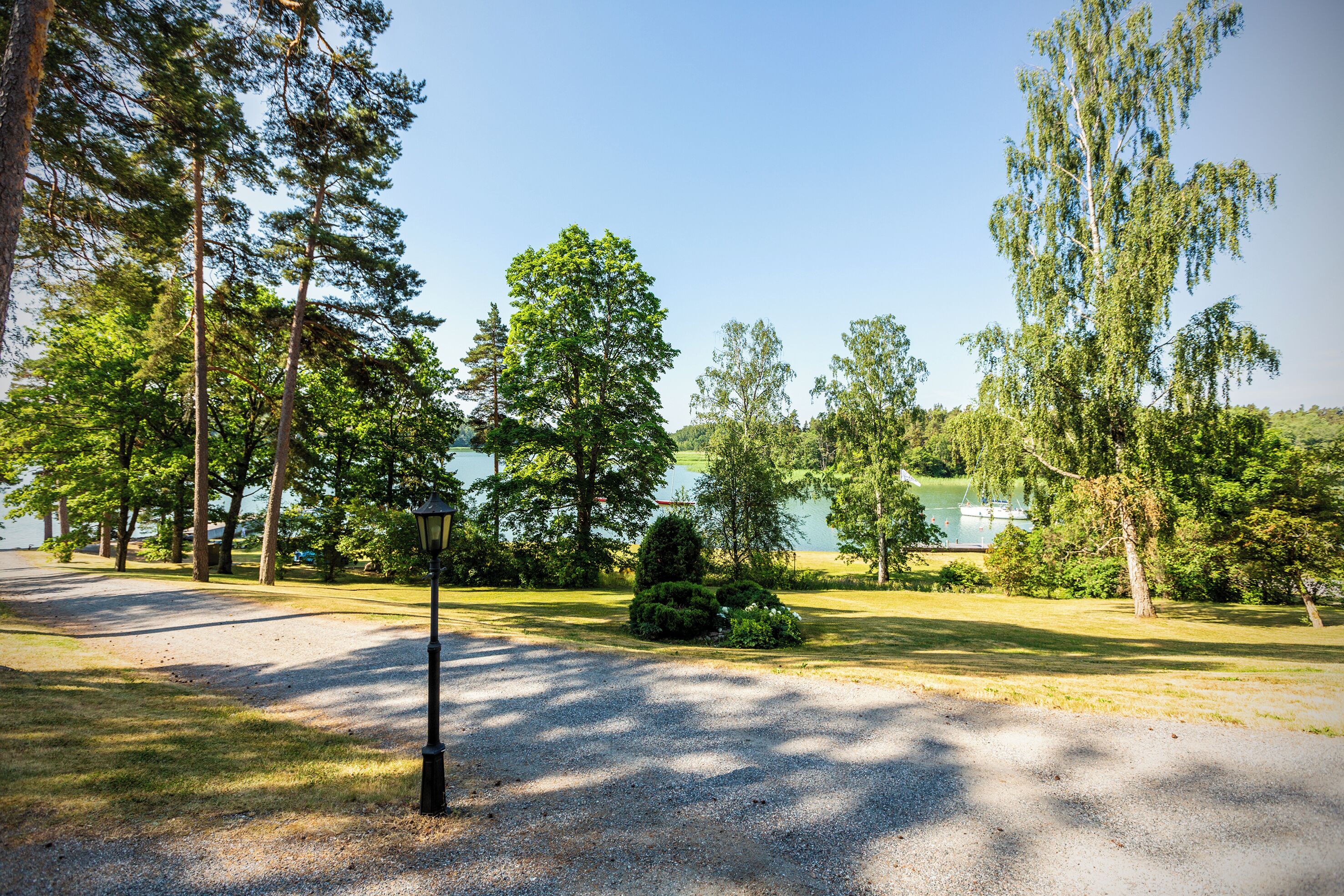 A park with a gravel path, trees, and a lamp post.