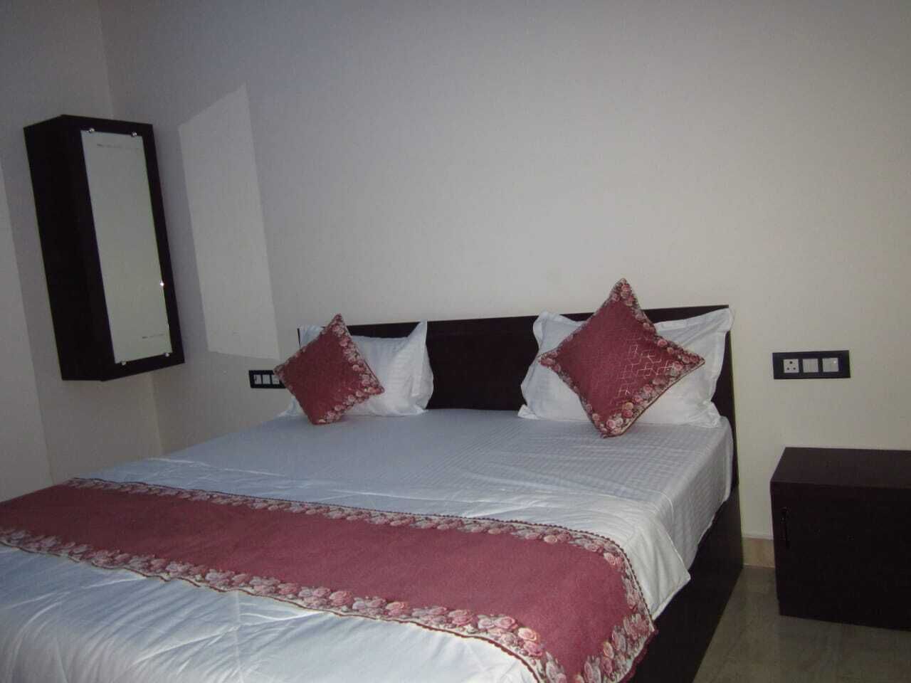 Un lit bien fait, recouvert d’une couette blanche et rouge, avec deux oreillers rouges et un plaid assorti de la même couleur.